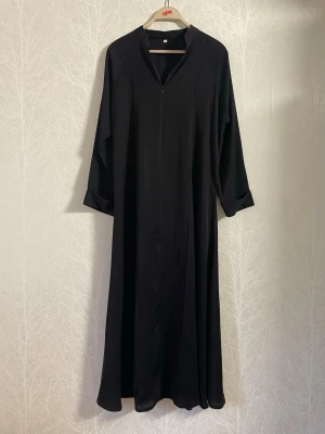 Svart Silky Abaya från Saudiarabien - Säljer en svart, silky abaya i storlek 52. Storleken avser endast längd (52 inches), så uppskattningvis passar den in i strl XS–M. Använd få gånger och är som ny. Köpt från Saudiarabien. Abayan kan bäras som stängd modell, eller öppen, men då behöver man justera den nerifrån så att dragkedjan går hela vägen ner.  Längd: ca 132 cm. Ärmlängd: ca 66 cm. Passar de som är under 160 cm.