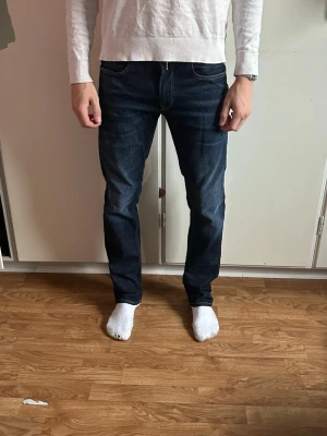 Mörkblå Replay Hyperflex jeans - Snygga mörkblå jeans från Replay Hyperflex med klassisk femficksdesign och kontrastsömmar. Jeansen har en slim fit passform och är tillverkade i stretchigt denim för extra komfort. Perfekta för dig som vill ha både stil och rörelsefrihet. Mannen på bilden är 180 cm och 67 kg