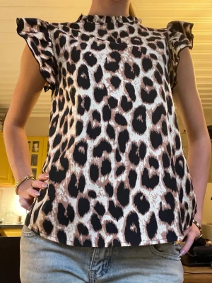 Leopardmönstrad blus med volangärm - Snygg blus med leopardmönster och volangdetaljer vid ärmarna. Modellen är ärmlös med rund halsringning och har en loose passform. Perfekt för dig som vill sticka ut med ett djurmönster i garderoben.