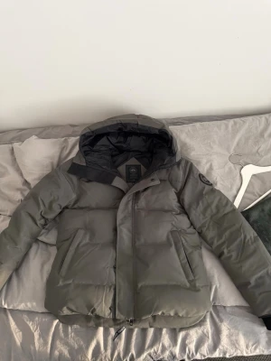 Canada goose macmillan blacklabel - Snygg grå pufferjacka från Canada Goose  med huva och två stora framfickor. Jackan har en diskret logotyp på ärmen och dragkedja framtill. Perfekt för kalla vinterdagar och riktigt varm tack vare sitt tjocka material. Jackan köpt föra vintern, säljer den eftersom att den inte passar längre och inte min stil längre, bra o köpa innan dom kalla vinterdagarna kommer. Skriv om du har minsta lilla fundering.