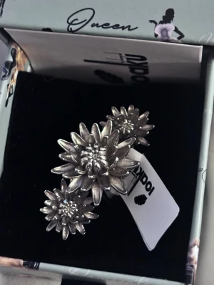 Silvrig ring med edelweissblommor - Unik silvrig ring med tre detaljerade edelweissblommor i olika storlekar. Ringen har en blank finish och är designad för att täcka två fingrar.  Köpt from ioaku från kids brand store, använt bara en gång så i nästan helt nytt skick 