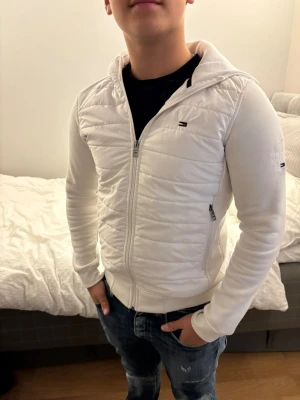 Vit quiltad hoodiejacka - Tommy Hilfiger Cardigan i mycket bra skick, passar folk mellan 168-178, Köptes av min kompis och använd helt okej ofta, själv har jag inte märkt några hål eller liknande på den