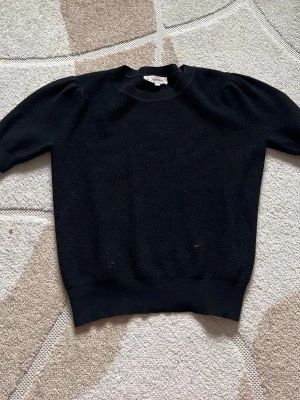 Svart stickad tröja med puffärm - Säljer en svart stickad tröja med puffärm och ribbade muddar vid ärmslut och nederkant. Tröjan har en klassisk rund halsringning och är gjord i mjukt material som känns skönt mot huden. Perfekt för dig som gillar enkel men trendig stil.