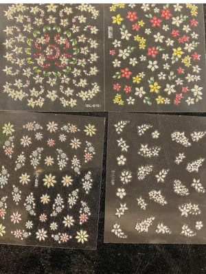 Blommiga nageldekaler i mixade färger - Ett set med flera ark nageldekaler med blommotiv i olika färger och former. Motiven inkluderar vita, rosa, gula och svarta blommor samt blad och hjärtan. Perfekt för att skapa kreativa och personliga nageldesigner. Tillverkade i tunt plastmaterial som är enkla att applicera.  45kr/4ark/bild 