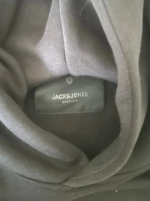 Svart hoodie Jack & Jones DO NOT DISTURB - Svart hoodie från Jack & Jones med stor vit text 'DO NOT DISTURB' på framsidan. Klassisk huva och avslappnad passform. Tillverkad i mjukt material som passar perfekt för chill dagar. Snygg och enkel design med tryck och används mindre än 3 gånger. 