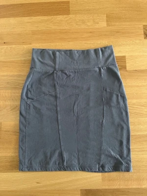 Grå kortkjol i bomull - En enkel och stilren grå kortkjol i mjukt bomullstyg. Kjolen har bred linning och diskreta sömdetaljer framtill som ger en snygg form. Perfekt att matcha med en t-shirt eller hoodie för en avslappnad look.
