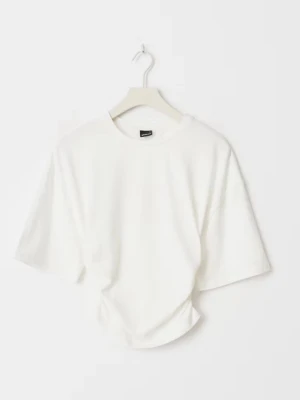 Vit croppad t-shirt med snörning - Säljer en vit croppad t-shirt med snörning i sidan som ger en snygg rynkad effekt. T-shirten har korta ärmar och rund halsringning. Perfekt till jeans eller kjol för en trendig look.