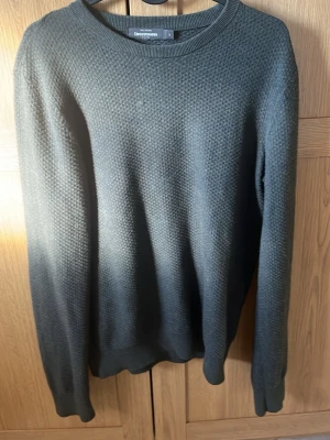 Mörkgrå stickad tröja Dressmann - Snygg mörkgrå stickad tröja från Dressmann i storlek S. Tröjan har rund halsringning, diskret strukturmönster och ribbade muddar vid ärmslut och nederkant. Perfekt för dig som gillar en enkel men stilren look.