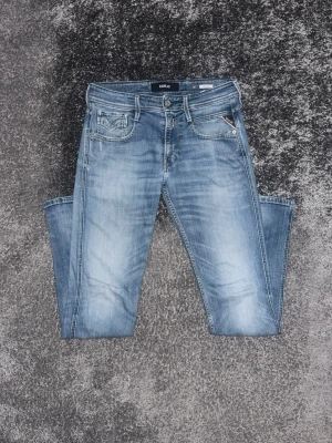 Ljusblå jeans från Replay - Snygga ljusblå jeans från Replay med klassisk femficksmodell och diskreta slitningar. Jeansen har raka ben och detaljerade sömmar, samt en liten logotyp på myntfickan. Perfekta för en avslappnad och trendig look.