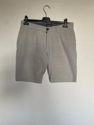 MANGUUN Linneshorts Herr | Beige | Storlek 31   - Snygga sommarshorts från MANGUUN i beige färg.                                              •Storlek: 31                                        •Material: 55% Lin / 45% Bomull. Skönt och luftigt linneblandning.                   •Skick: Välbevarade och har inga tecken på slitage. Inga hål eller fläckar   Supersnygga till skjorta, piké eller t-shirt på sommaren. Linnetyget gör att de är svala att bära.