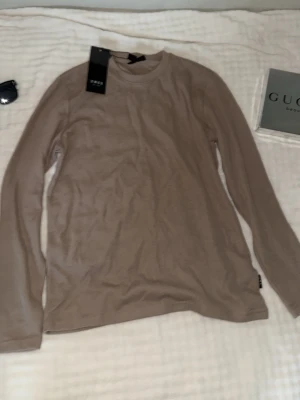 Beige långärmad topp från SMOG - Säljer en stilren beige långärmad topp från SMOG. Toppen har rund halsringning och är tillverkad i mjuk bomull som känns skön mot huden. Perfekt att matcha med jeans eller kjol för en clean look.