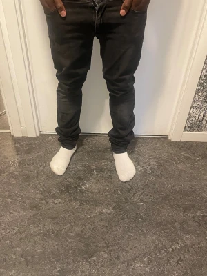 Svarta slim fit jeans - Säljer ett par svarta slim fit jeans med lätt tvättad look. Jeansen har klassisk femficksdesign och normal midja. Passformen är smal hela vägen ner och materialet är troligtvis bomull med lite stretch för extra komfort.