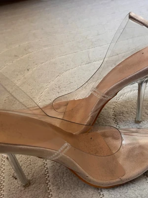 Transparenta pumps med klack - Säljer ett par trendiga transparenta pumps med hög klack i akryl och genomskinliga plastdetaljer. Skorna har en spetsig tå och en stilren design som ger en modern look. Perfekta för dig som vill ha ett par statement heels till din outfit.