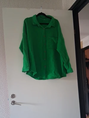 Grön oversized skjorta med knappar - Säljer en grön oversized skjorta i mjukt, strukturerat tyg. Skjortan har långa ärmar, klassisk krage, bröstficka och knäppning framtill. Perfekt för en avslappnad och trendig look. Vid armhålan så e det ett hål som e fixad med lim för kläder