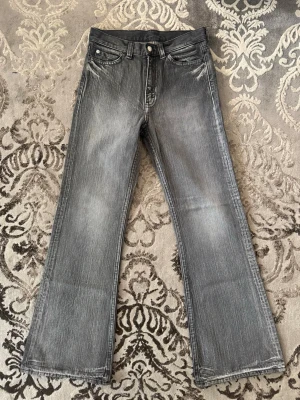 Grå bootcut jeans med slitningar - Säljer ett par grå bootcut jeans från märket Cheap Monday med snygga slitningar och klassisk femficksmodell. Jeansen har en lätt utsvängd passform och detaljerade sömmar. Materialet är denim och färgen är tvättad grå med ljusare partier för en cool vintage-look. De sitter som 28/32. Kontakta vid minsta fundering. 