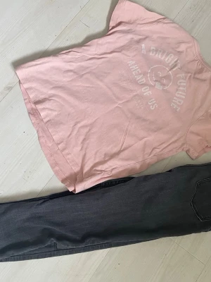 Ljusrosa t-shirt med tryck - Säljer en ljusrosa t-shirt med ett diskret tryck på bröstet där det står 'A BRIGHT FUTURE AHEAD OF US' och en smiley. T-shirten har rund hals och korta ärmar. Perfekt basic-plagg i mjuk bomull som passar till allt.samt Jegginsbbpfs i storlek 134-140