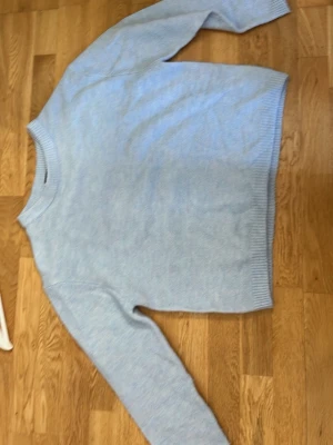 Ljusblå stickad tröja från 157 - Mysig ljusblå stickad tröja från 157 med rund halsringning och ribbade muddar vid ärmslut och nederkant. Perfekt för kyliga dagar och enkel att matcha med jeans eller kjol.