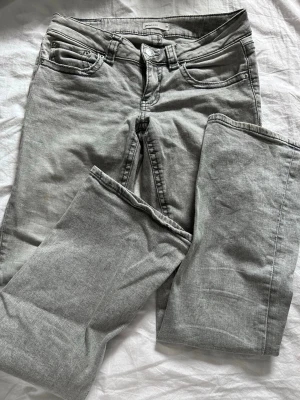 Gråa bootcut jeans med ficklock - Snygga grå jeans med bootcut-modell och coola ficklock bak. Jeansen har klassisk femficksdesign, knappgylf och är tillverkade i mjukt denimtyg. Perfekta för dig som gillar en avslappnad men trendig stil.