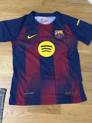 Barcelona matchtröja Joao Cancelo - Snygg FC Barcelona matchtröja i blått och vinrött med gula detaljer. Tröjan har klubbmärke, Nike-logga och Spotify som sponsor framtill. På ryggen står det Joao Cancelo och nummer 2 i gult. Tillverkad i lätt och ventilerande material, perfekt för fotboll.