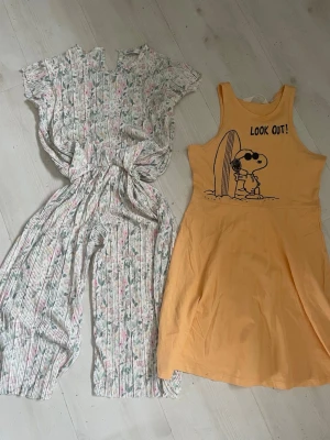 Gul klänning med Snoopy-tryck - Gul ärmlös klänning med tryck av Snoopy och texten 'LOOK OUT!' framtill. Klänningen har rund halsringning och är i mjukt material, perfekt för varma dagar. Lätt och bekväm modell med avslappnad passform.     Byxor och topp i ett ljus  med blommigt mönster  I polyester  