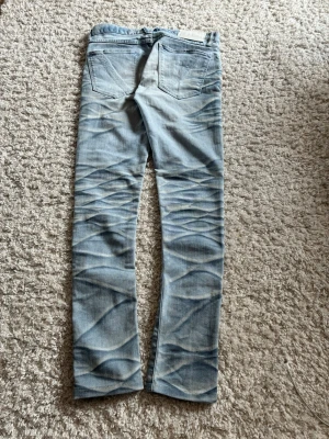 Ljusblå jeans från Vanquish - Säljer ett par ljusblå jeans från Vanquish med snygg tvätt och unika slitningar på benen. Jeansen har raka ben, klassiska bakfickor och är tillverkade i bomull. Perfekta för dig som gillar streetwear och vill sticka ut lite extra. Vanquish washed jeans i bought these from japan 