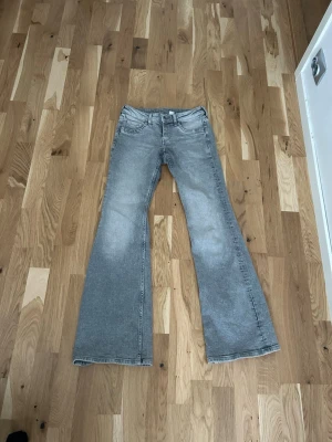 Gråa utsvängda jeans - Säljer ett par gråa jeans med utsvängda ben och klassisk femficksmodell. Jeansen har en tvättad look och normal midja. Perfekta för dig som gillar retrostil och vill ha ett par riktigt snygga jeans med breda ben.