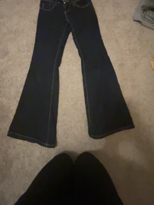 Mörkblå bootcut jeans - Säljer ett par mörkblå bootcut jeans med klassisk femficksmodell och kontrastsömmar. Jeansen har hög midja och vida ben som ger en snygg retrovibe. Perfekta att styla med sneakers eller boots för en cool look.
