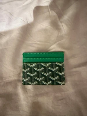 Grön kortfodral med mönster - Snyggt kortfodral i grönt med ett ikoniskt grafiskt mönster i vitt och svart. Fodralet har flera kortfack och är gjort i ett glansigt material som ser ut som läder eller canvas. Perfekt för dig som vill ha en stilren och trendig accessoar.