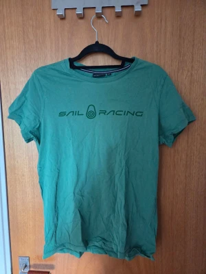 Grön Sail Racing t-shirt - Snygg grön t-shirt från Sail Racing med tryck på bröstet. Klassisk passform och rund halsringning. Perfekt till jeans eller shorts för en avslappnad stil.