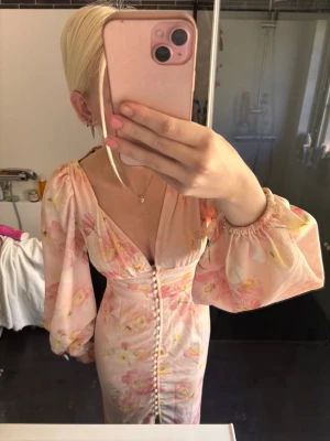 Ljus blommig långklänning med puffärm - Romantisk långklänning i ljusa toner med blommigt mönster. Klänningen har djup v-ringning, puffiga långärmar och knappar framtill. Materialet ser ut att vara lätt och luftigt, perfekt för varma dagar. Snygg passform som markerar midjan. Stl 34 och bara använd några ggr 