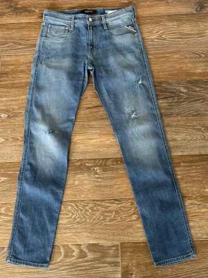 Replay Anbass Slim Fit  - Säljer ett par blå Replay Anbass slim fit jeans med slitningar och snygg tvätt. Klassisk femficksmodell med dragkedja och knapp. Jeansen har Replay-logga på myntfickan och är tillverkade i mjuk denim med stretch för extra komfort. Endast använda 1 gång