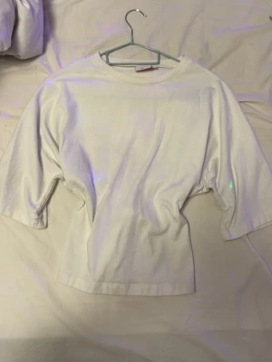 Vit topp med knyt i ryggen - Säljer en vit topp med rund hals och halvlånga ärmar. Toppen har en unik detalj med knyt i ryggen som ger en snygg twist. Tillverkad i mjuk bomull som känns skön mot huden. 