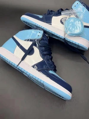 Jordan 1 UNC  - Säljer ett par riktigt snygga höga sneakers i marinblått, ljusblått och vitt. Skorna har glansig finish, klassisk snörning och en kontrasterande sula i ljusblått. Perfekta för dig som vill sticka ut med din stil och gillar sportig vibe.