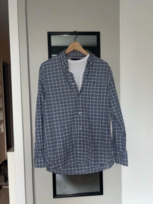 Blårutig skjorta från Tommy Hilfigher - Snygg Tommy Hilfigher skjorta i blått och vitt rutmönster med button down krage. Perfekt för en avslappnad men stilren look.