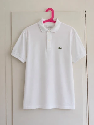 Vit klassisk Lacoste-piké 🤍🐊 - Stilren vit pikétröja från Lacoste med den klassiska broderade krokodilloggan på bröstet. Perfekt till både vardag och lite finare tillfällen. • Storlek: 12 år / 152 cm • Färg: Vit • Kortärmad modell med krage och knappar • Mycket fint skick men den är lite missfärgad!😁 Säljer då den inte kommer till användning längre. Hör gärna av dig vid frågor eller om du vill ha fler bilder! 💕