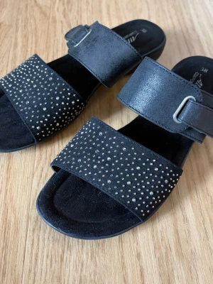 Svarta sandaler med strass - Snygga svarta sandaler med två breda remmar, varav den främre är dekorerad med små silverfärgade strass. Remmarna är i mockaimitation och har ett spänne på sidan för justering.