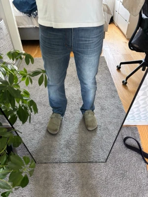 Blå raka jeans med rå kant - Säljer ett par blå jeans med rak passform och rå, avklippt kant vid bensluten. Jeansen har klassisk femficksdesign och slitningar framtill för en avslappnad look. Perfekta för dig som gillar en lite mer edgy stil.