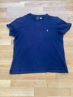 Mörkblå t-shirt från Polo Ralph Lauren - Snygg mörkblå t-shirt från Polo Ralph Lauren med klassisk passform och rund hals. T-shirten har den ikoniska lilla vita logotypen broderad på bröstet och är gjord i mjuk bomull. Perfekt till jeans eller shorts för en clean look. Otroligt svårhittad.