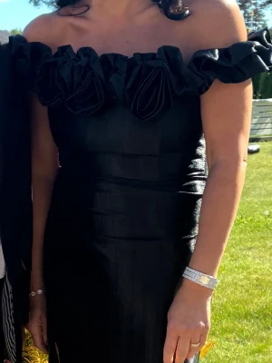 Svart axelbandslös klänning - Ombre DOROTEA – elegant svart festklänning  Säljer denna vackra svarta festklänning från Ombre, modell DOROTEA. En riktigt elegant off-shoulder-modell med vackra volang- och blomdetaljer upptill, figurnära överdel och lång kjol med slits framtill.  *Märke: Ombre *Modell: DOROTEA  *Storlek: XL, men upplevs snarare som ca storlek 40 ✨ Skick: Mycket fint skick – endast använd 1 gång 💰 Ordinarie pris: 3 335 kr 🏷️ Mitt pris: 1800 kr