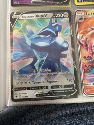 Pokémonkort Origin Forme Dialga V - Säljer ett Origin Forme Dialga V Pokémonkort med 220 HP. Kortet har en futuristisk design i blått och silver med holografiska effekter. Det har attackerna Metal Coating och Temporal Rupture. Perfekt för samlare eller Pokémon TCG-spelare.