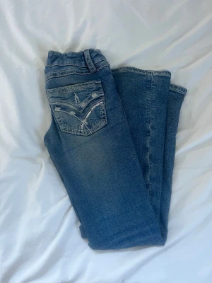 Blåa jeans med detaljer på dixkan - Blåa jeans med detaljer på fick från gina young. De är sköna men de saknar sina knappar på fickorna annars är de hela!