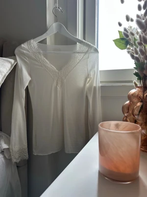 Vit långärmad topp med spetsdetaljer - Säljer en vit långärmad topp med v-ringning och fina spetsdetaljer vid halsringningen och ärmsluten. Toppen har en feminin och enkel design som passar perfekt till jeans eller kjol. Köpt på intimissimi. Storlek S. Säljer pga att jag köpte i fel färg. Endast använts 2 gånger💕