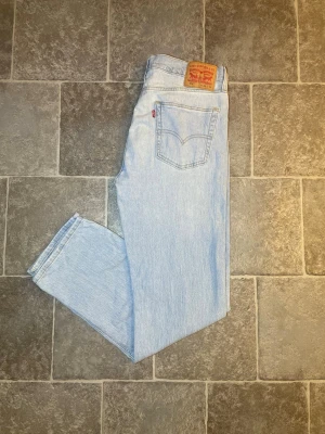 Ljusblå raka Levi's jeans - Säljer ett par klassiska ljusblå Levi's jeans med rak passform och fem fickor. Jeansen har den ikoniska läderlappen bak i midjan och röd Levi's-tagg på bakfickan. Tillverkade i slitstark denim, perfekta för en avslappnad och tidlös stil.