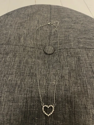 Silverfärgat halsband med hjärta - Snyggt halsband i silverfärg med en tunn kedja och ett hjärtformat hänge dekorerat med små pärlor. Perfekt accessoar för att lyfta din outfit med en söt och trendig detalj. (Obs, asken kommer inte med)🥰