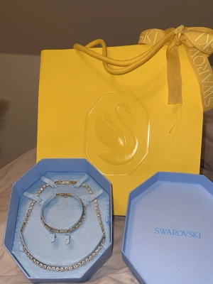 Swarovski set - Fint Swarovski smyckes set med armband och halsband. Matchande örhängen finns att köpa, bilder skickas vid förfrågan. Ingenting saknas, allting finns med. Påsen inkluderad ifall önskan till de finns (har därför lagt medelstor paket för att den ska få plats). Lite slitage på armbandet (visad på bilden) bara på undersidan som annars inte syns. Det går att både förlänga och förkorta halsbandet & armbandet. Guldpläterade i 18k guld.