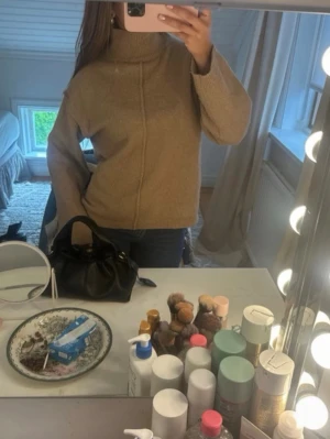 Beige stickad polotröja - Säljer en beige stickad polotröja med hög krage och raka ärmar. Tröjan har en avslappnad passform och en synlig söm framtill som detalj. Perfekt för kyliga dagar och enkel att matcha med jeans eller kjol.