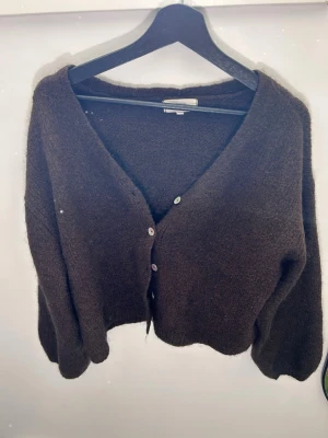 Mörkbrun fluffig kofta - Mysig mörkbrun kofta med v-ringning och 5 knappar framtill. Koftan har en fluffig, mjuk struktur och långa ärmar. Den är från Gina tricot och är i storlek S