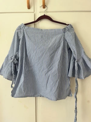 Blå randig blus - Så söt blå randig off shoulder som man knyter i ärmarna. Helt nytt skick säljer då jag inte använt den nåt. Off shoulder sitter på bra sätt och far inte upp hela tiden som andra off shoulder är.