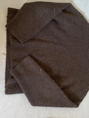 Mörkbrun stickad tröja - Mysig mörkbrun stickad tröja med lång ärm och ribbstickade muddar vid ärmslut och nederkant. Tröjan har en enkel, rak passform och är gjord i ett fluffigt, mjukt material som ser ut att vara ull eller mohair.