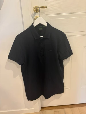 Hugo boss pike - Säljer min Hugo Boss piké i mörkblå färg, som nästan ser svart ut. Har en snygg grön Hugo Boss-logga på bröstet. Stilren och enkel piké som passar både till vardags och lite finare tillfällen.